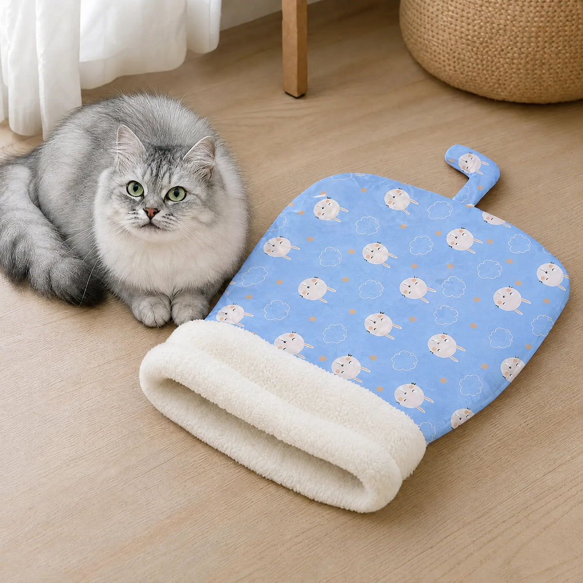 Gatto disteso sul pavimento accanto al sacco a pelo azzurro con fantasia a pecorelle